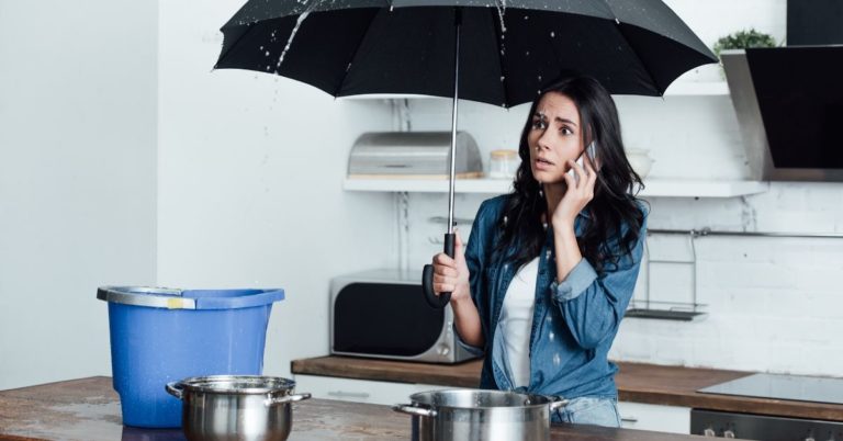 Can I Get a Personal Loan with Bad Credit - picture of woman on phone holding umbrella over kitchen counter with water pouring down from ceiling