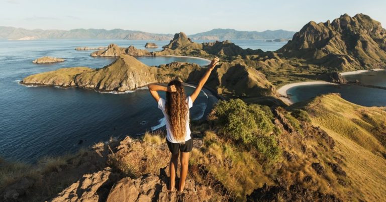 How to Pay Off Debt and Start Traveling - picture of back of woman overlooking mountains and water with arm raised