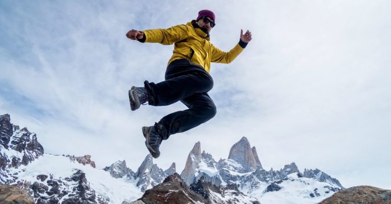 MG Travel Insurance Review - picture of man jumping in air on mountain top