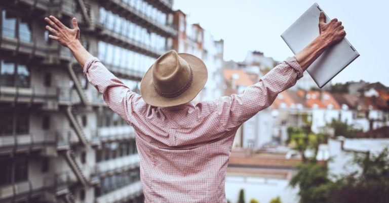 Keys to Surviving and Thriving with a Freelance Income - picture of back of man with laptop in one hand with arms raised