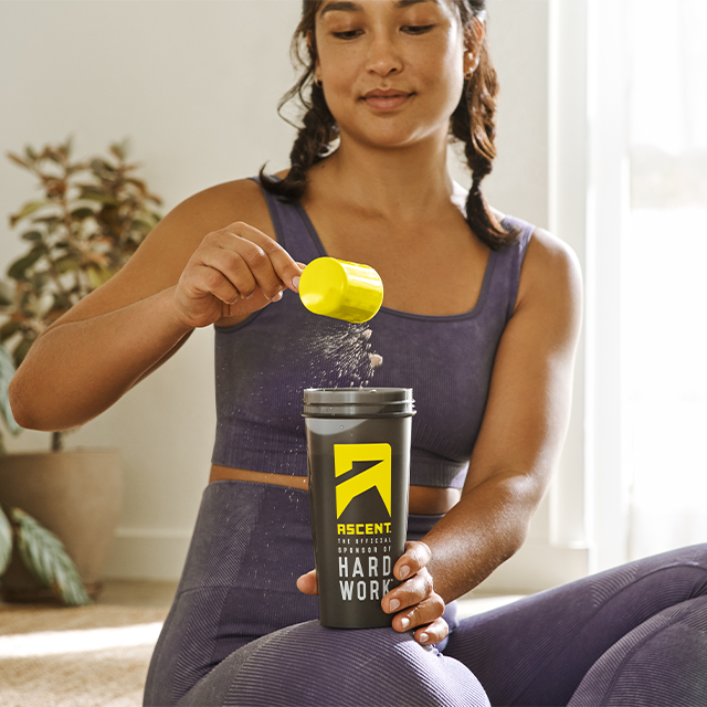 ascent protein athlete scooping protein powder into a blender bottle